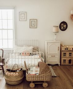 a bedroom with white walls and wooden floors, including a wicker baby carriage in the foreground