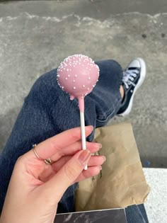 a person holding a pink lollipop with white sprinkles on it