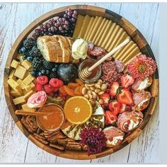 a wooden platter filled with different types of cheeses, fruit and crackers