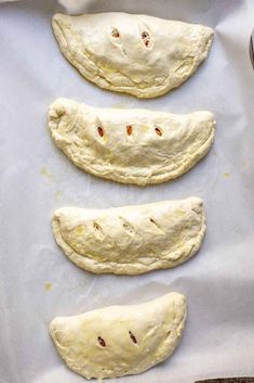 four uncooked pizza doughs on a baking sheet