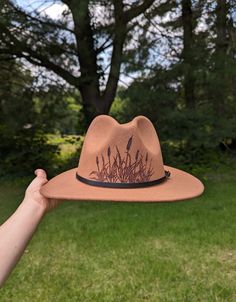 This fedora makes a great addition to any wardrobe. The warm brown material burns a gorgeous shade of dark brown allowing the design to stand out. Cattails are are intricately burned by hand with a pyrography machine. This cattail design is burnt on the front of the crown. All my designs are original and completely freehanded. For a beautiful finishing touch the hat is adorned with a faux leather black hatband. Hat Materials: 65%cotton 35% polyester Hat fits most women with an adjustable tie band inside *Disclaimer* Colors may vary slightly from screen to screen Adjustable Brown Fedora Felt Hat, Brown Brimmed Hat For Festivals, Brown Fedora With Short Brim For Country Events, Brown Country Hat With Short Brim, Brown Outdoor Cap Felt Hat, Adjustable Brown Hat With Curved Brim, Brown Flat Brim Fedora For Rodeo, Brown Short Brim Country Hat, Brown Felt Cap For Outdoor