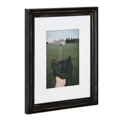 a baseball glove sitting on top of a field in front of a white wall with a black frame