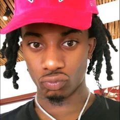 a man with dreadlocks wearing a pink baseball cap and looking at the camera