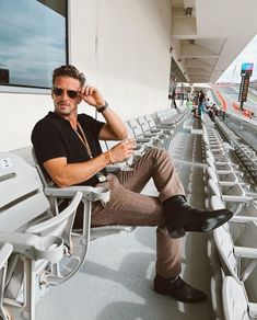 a man in black shirt and brown pants sitting on a white chair with his legs crossed