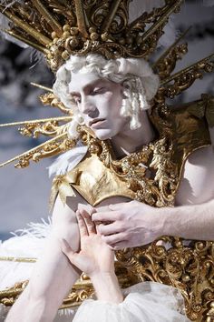 a man dressed in white and gold with his hands on his chest while holding something