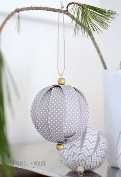 two ornaments are hanging from a tree branch in front of a white vase with pine branches