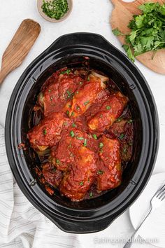 a slow cooker filled with meat covered in sauce and garnished with parsley