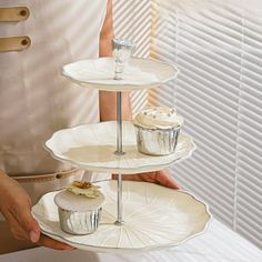 two tiered trays with cupcakes on them being held by someone's hand