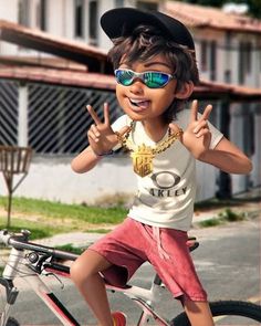 a young boy wearing sunglasses and standing on top of a bike giving the peace sign