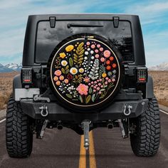 a black jeep with flowers painted on the front and back tire cover is parked in a parking lot