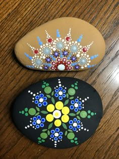 two painted rocks sitting on top of a wooden table next to each other and one has a flower design