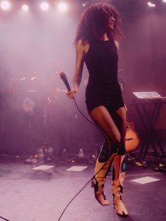 a woman standing on top of a stage with a microphone in her hand and wearing boots