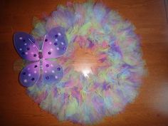 a purple and blue butterfly sitting on top of a white wreath with feathers around it