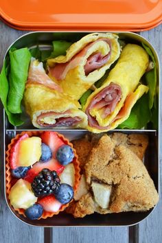 an open lunch box with fruit and muffins