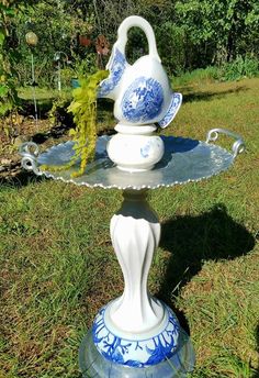 a blue and white vase sitting on top of a metal stand in the grass next to trees