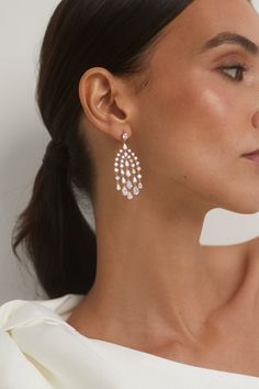 a woman wearing large white earrings with crystal drops on the bottom and back of her ear