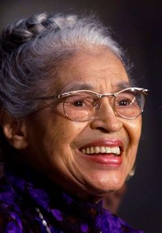 an older woman wearing glasses and a purple scarf smiles at the camera while standing in front of a black background