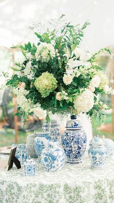 a vase with white flowers and green leaves sits on a blue and white tablecloth