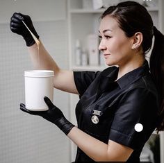 a woman in black shirt and gloves holding a white cup