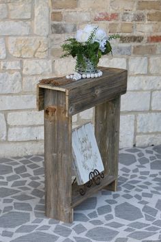 a vase with flowers sitting on top of a wooden table next to a brick wall