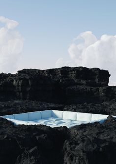 an iceberg in the middle of some black rocks with clouds and blue sky behind it