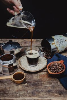 a person pouring coffee into a cup on top of a wooden table next to other items