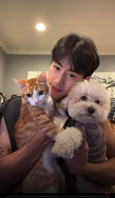 a young man holding a cat and dog in his arms while smiling at the camera