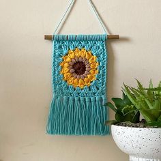 a wall hanging with a crocheted sunflower on it next to a potted plant