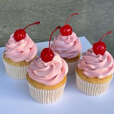 three cupcakes with pink frosting and cherries on top are sitting next to each other