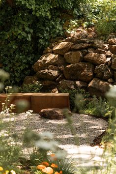 there is a bench in the middle of some plants and rocks near a rock wall