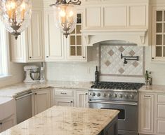 a kitchen with white cabinets and marble counter tops, two chandeliers above the stove