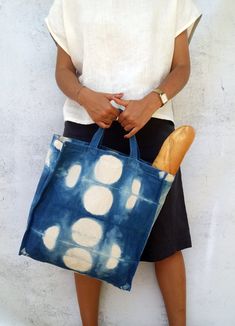 a woman holding a blue bag with white dots on it and a loaf of bread in her hand