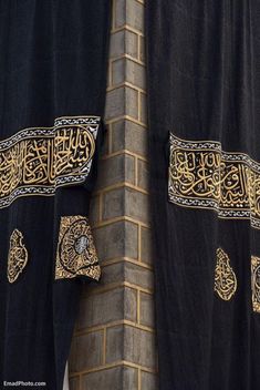 two black and gold curtains with arabic writing on them hanging from the side of a brick building