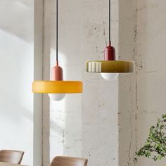 three different colored lights hanging from the ceiling in a room with white walls and wooden chairs