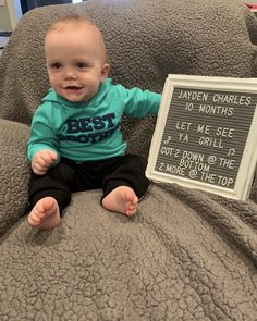 a baby sitting on top of a couch next to a sign