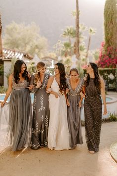 a group of women standing next to each other in front of a pool and palm trees