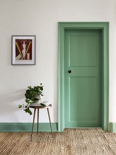 a green door in the corner of a room next to a table with a potted plant on it