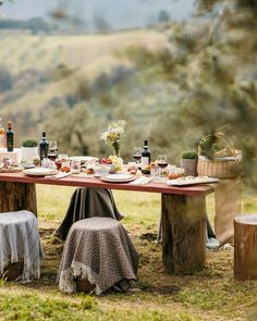 a picnic table set up with plates and wine bottles on it in the middle of a field