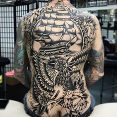 the back of a man's body with an eagle and ship tattoo on it