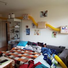 an unmade bed in a room with pictures on the wall and shelves above it