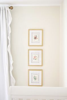 three framed pictures hang on the wall above a crib in a white nursery room