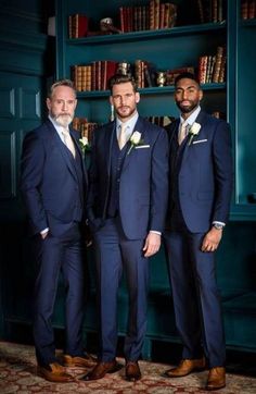 three men in suits and ties standing next to each other near bookshelves with shelves full of books behind them