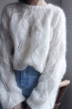 a woman wearing a white sweater and denim shorts is sitting in a chair with her hands on her hips