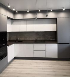 an empty kitchen with white cabinets and black counter tops is seen in this image, there are lights hanging from the ceiling