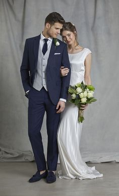 a bride and groom pose for a wedding photo in front of a gray backdrop with white flowers