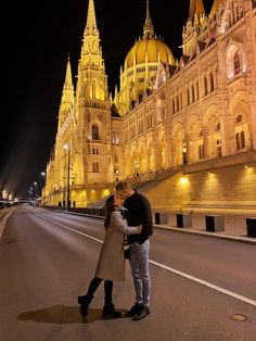 a man and woman kissing on the street in front of an ornate building at night