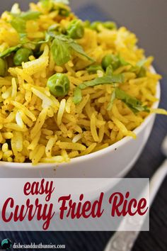 a white bowl filled with yellow rice and green vegetables next to a fork on a blue place mat