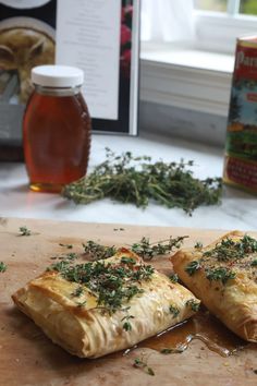 two pastries sitting on top of a cutting board next to a jar of honey