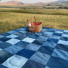 a picnic blanket with a basket and bottle on it in the middle of a field