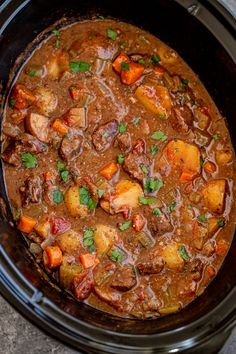 a crock pot filled with beef stew and potatoes, garnished with parsley